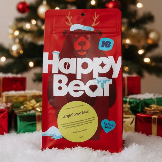 Red 'Happy Bear' package with a Christmas tree and decorations in the background